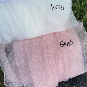 May include: Four swatches of sparkly tulle fabric in white, ivory, blush, and black. The fabric is layered with the white swatch on top and the black swatch on the bottom.
