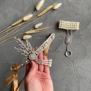 May include: A silver headband with rhinestones and pearls, a gold ribbon, and a matching pearl bracelet with a silver charm.