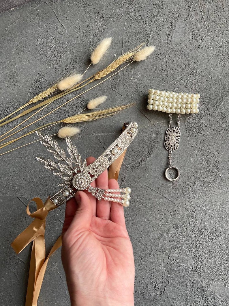 May include: A silver headband with rhinestones and pearls, a gold ribbon, and a matching pearl bracelet with a silver charm.