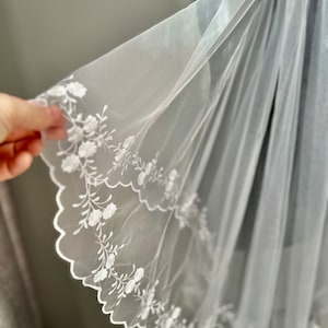 Peut inclure: Voile de mariée blanche avec une délicate broderie florale et des bords festonnés.