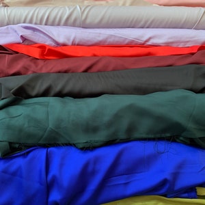 May include: A stack of fabric rolls in various colors, including white, pink, lavender, red, burgundy, black, green, blue, and yellow.