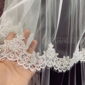 May include: White bridal veil with a delicate lace trim. The lace features a floral pattern.