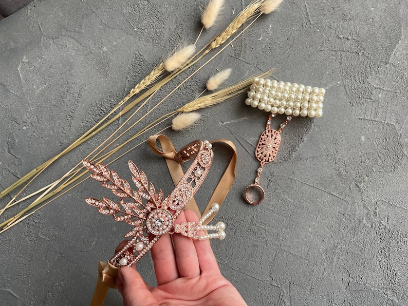May include: A set of two gold-toned headbands with pearl and crystal embellishments. One headband is a delicate chain with a floral design and the other is a simple band with pearls.