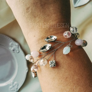 May include: A delicate bracelet with a silver wire base and a variety of crystal and glass beads in shades of pink, white, and clear. The bracelet features a few larger crystal beads in a teardrop shape.
