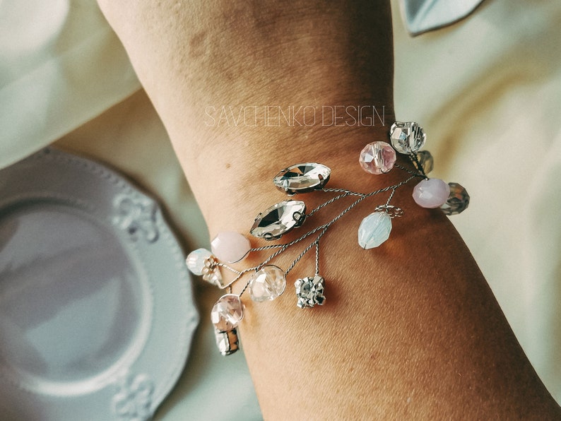 May include: A delicate bracelet with a silver wire base and a variety of crystal and glass beads in shades of pink, white, and clear. The bracelet features a few larger crystal beads in a teardrop shape.