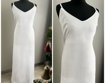 May include: A white, sleeveless maxi dress with a V-neckline. The dress is made of a silky fabric and has a simple, elegant design.