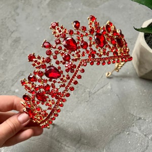 Op de afbeelding: Een gouden kroon met rode edelstenen. De kroon is versierd met ingewikkelde details en heeft een puntige top.