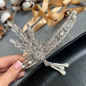 May include: A silver headband with a pearl and rhinestone design. The headband has a leaf-like design on one side and a pearl drop on the other.