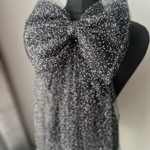May include: A large black bow made of tulle with white glitter dots. The bow is tied around a black mannequin.