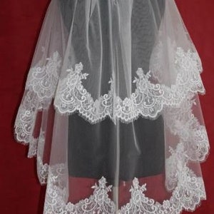 May include: A white bridal veil with three layers of lace trim. The veil is made of soft tulle and features delicate floral patterns.