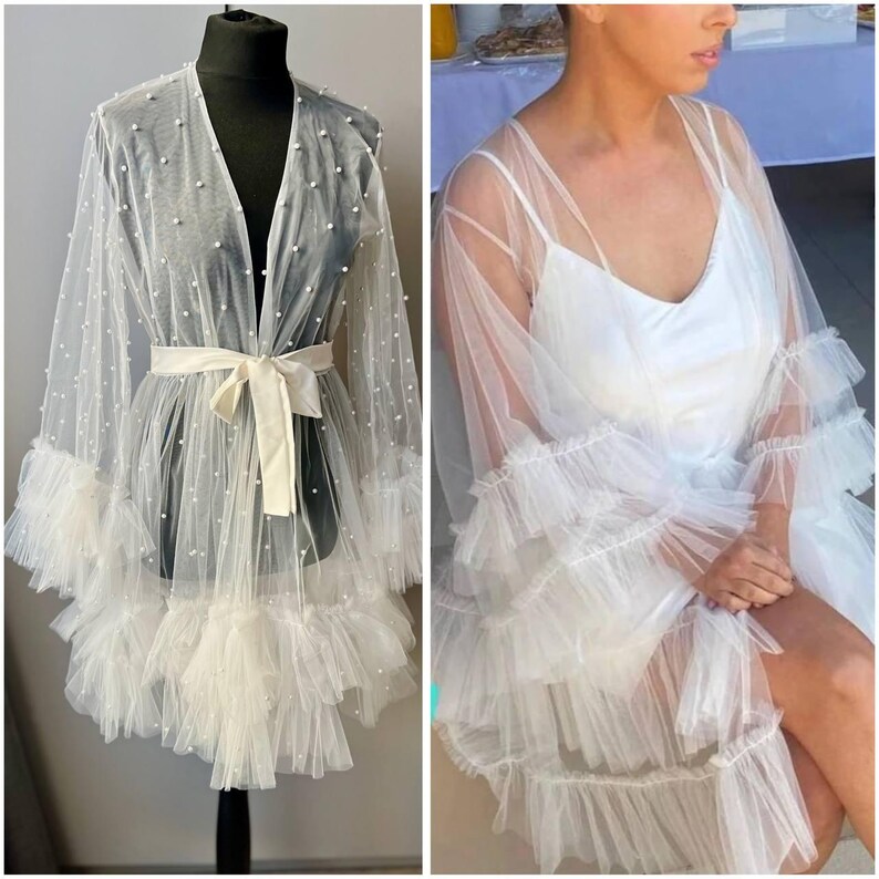 May include: A white sheer robe with pearl embellishments and ruffled trim. The robe has a tie at the waist and long sleeves.
