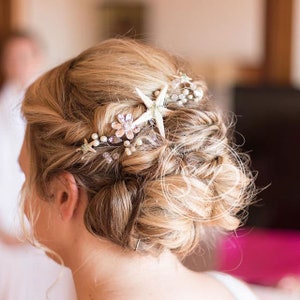 Può includere: I capelli di una sposa sono raccolti in uno chignon morbido con un pettine per capelli con perle e stelle marine. Il pettine presenta una stella marina bianca, perline di perle e strass.