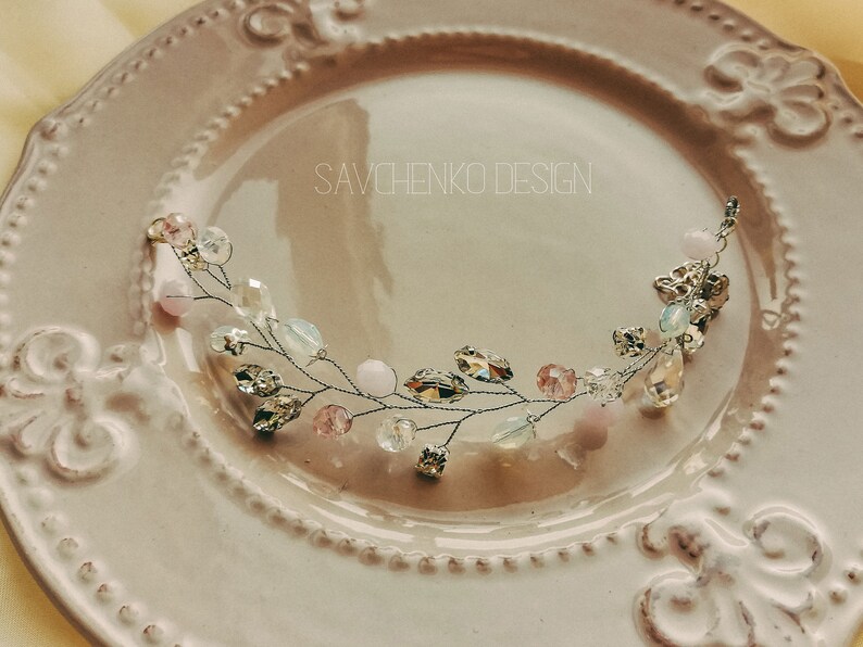 May include: A delicate silver wire hair comb with pink and clear glass beads and crystals. The comb is shaped like a branch with leaves and flowers.