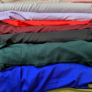 May include: A stack of fabric swatches in various colours, including white, beige, pink, lavender, red, burgundy, black, green, blue, and yellow.