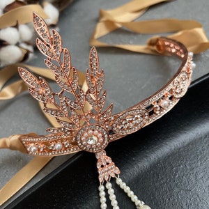 May include: A rose gold headband with a delicate design of leaves and rhinestones. The headband has a pearl drop pendant and is adorned with small pearls.