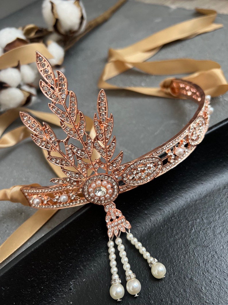 May include: A rose gold headband with a delicate design of leaves and rhinestones. The headband has a pearl drop pendant and is adorned with small pearls.