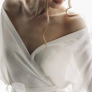 May include: A white satin robe with a wrap style and a tie at the waist. The robe has long sleeves and a deep V-neckline.