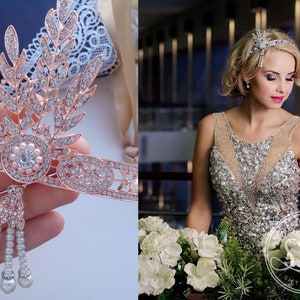 May include: A rose gold headband with a delicate floral design and pearl accents. The headband is adorned with sparkling rhinestones and features a dangling pearl drop.