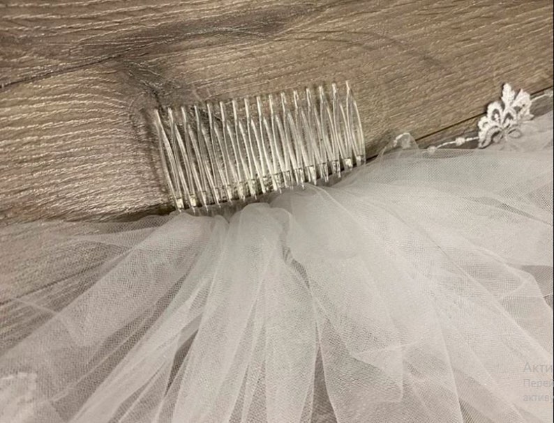 May include: A white tulle bridal veil with a comb attached to the top. The veil has a lace trim around the edge.