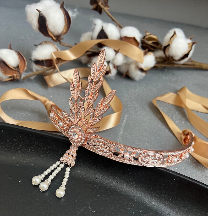 May include: Rose gold headband with a delicate leaf design and pearl accents. The headband has a small, dangling pearl tassel.