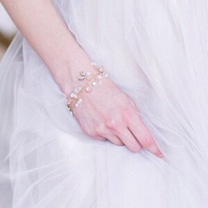 May include: A delicate gold bracelet with pink and white crystals arranged in a floral design. The bracelet is made of wire and has a delicate, feminine look.