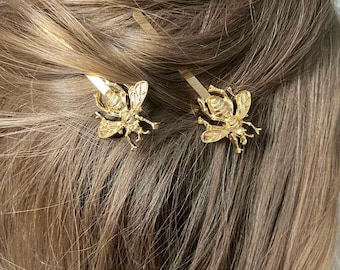May include: Two gold bee hair clips with detailed wings and bodies. The clips are in brown hair.