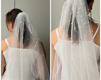 May include: A white bridal veil with pearl embellishments. The veil is made of tulle and is designed to be worn over a ponytail.
