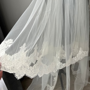 May include: A white tulle wedding veil with a delicate lace trim. The veil is soft and flowing, and the lace trim adds a touch of elegance.