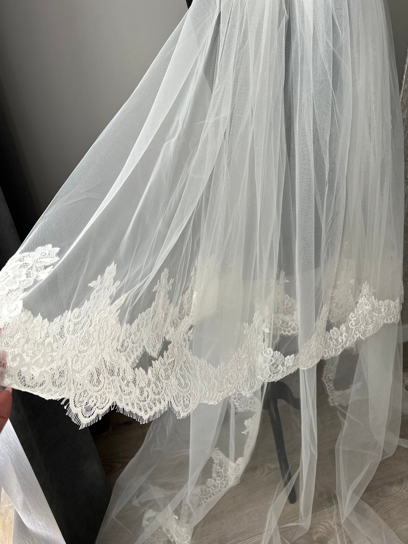 May include: A white tulle wedding veil with a delicate lace trim. The veil is soft and flowing, and the lace trim adds a touch of elegance.