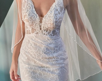 May include: A white lace wedding dress with a plunging neckline and a veil with a beaded edge.