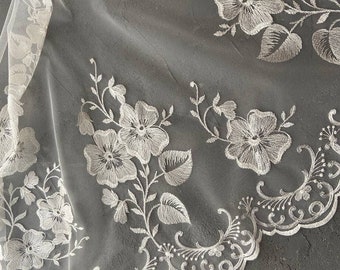 May include: White floral lace fabric with a scalloped edge. The lace is delicate and intricate, with a floral pattern that is repeated throughout the fabric.