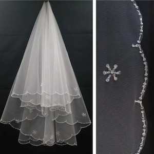 May include: A white bridal veil with a scalloped edge and delicate floral beading. The veil has three layers and is decorated with small, sparkling sequins.