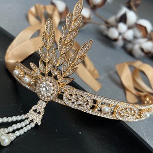May include: A gold headband with a delicate design of leaves and rhinestones. The headband is adorned with small white pearls and has a dangling pearl tassel.