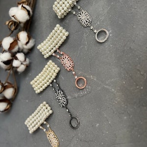 May include: Four pearl bracelets with a rhinestone ring attached to each. The bracelets are white and the rings are silver, rose gold, black, and gold.