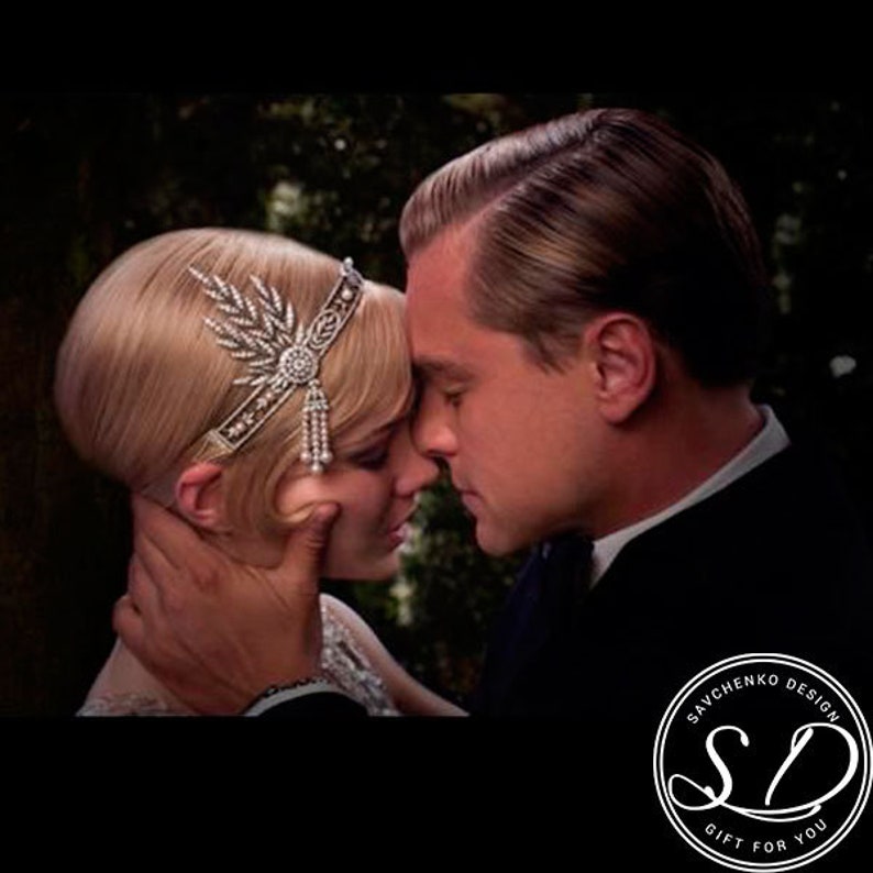 May include: A black and white photo of a couple looking at each other. The woman is wearing a headband with a pearl and crystal design. The man is wearing a suit and tie. The photo is cropped to show only the couple's faces and shoulders.