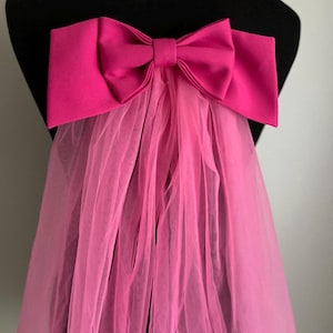 Op de afbeelding: Een roze tule sluier met een grote roze satijnen strik aan de bovenkant.