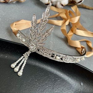 May include: A silver headband with a pearl and rhinestone design. The headband has a delicate, leaf-like design and a dangling pearl strand.
