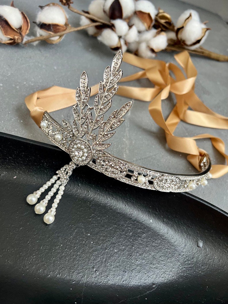 May include: A silver headband with a pearl and rhinestone design. The headband has a delicate, leaf-like design and a dangling pearl strand.