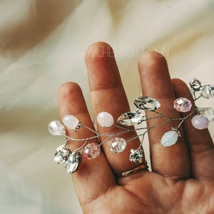May include: A delicate silver wire hair vine with clear, pink, and white crystal beads. The vine is held in a hand, with the text "SAVCHENKO DESIGN" visible in the background.
