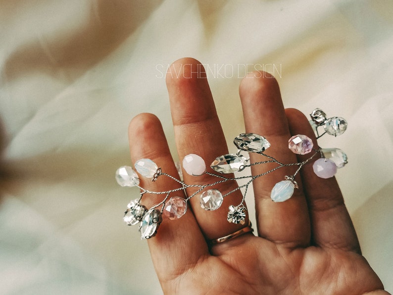May include: A delicate silver wire hair vine with clear, pink, and white crystal beads. The vine is held in a hand, with the text "SAVCHENKO DESIGN" visible in the background.