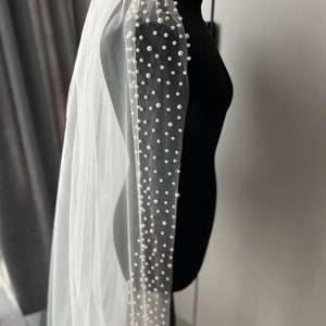 May include: A white tulle wedding veil with a single row of pearl embellishments along the edge.