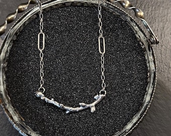 Può includere: Una collana d'argento con un delicato designo a forma di ramo. La catena è composta da piccoli cerchi collegati. Il ciondolo a forma di ramo ha un aspetto naturale e organico.