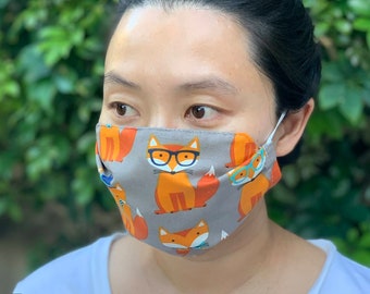 May include: A person wearing a gray face mask with a repeating pattern of orange foxes wearing glasses. The text "DIAMOND CITY CO." is visible on the bottom right of the image. The text "Fox" is visible on the bottom left of the image.