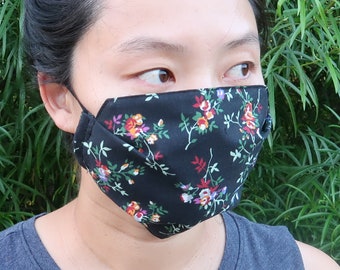 Puede incluir: Una mascarilla negra con un estampado floral en rojo, rosa, naranja y blanco. La mascarilla tiene cintas elásticas negras para las orejas y está hecha de tela. El texto "Black Floral" está en la parte inferior de la imagen.