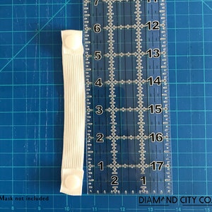 K&ouml;nnte beinhalten: Wei&szlig;es Gummiband mit zwei wei&szlig;en Plastikkn&ouml;pfen. Das Band wird an einem Lineal gemessen und ist etwa 7,6 cm lang.