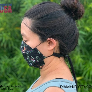 Puede incluir: Una mascarilla facial negra con estampado floral y correas ajustables. La mascarilla est&aacute; hecha en los Estados Unidos y es de talla para adultos. El texto "DIAMOND CITY CO." es visible en la esquina inferior derecha de la imagen.