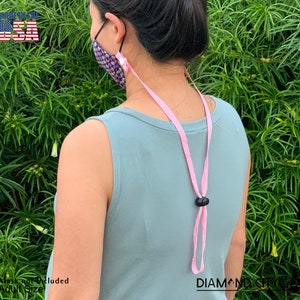 Puede incluir: Cord&oacute;n rosa para mascarilla facial con cierres de pl&aacute;stico negro. El cord&oacute;n est&aacute; hecho en los Estados Unidos. El texto "DIAMOND CITY CO." es visible en la esquina inferior derecha de la imagen.