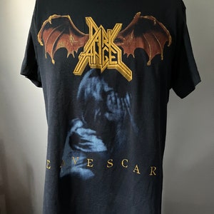 Puede incluir: Camiseta negra con un gr&aacute;fico dorado y marr&oacute;n de una banda llamada "Dark Angel" con las palabras "Eavescar" impresas debajo del gr&aacute;fico.