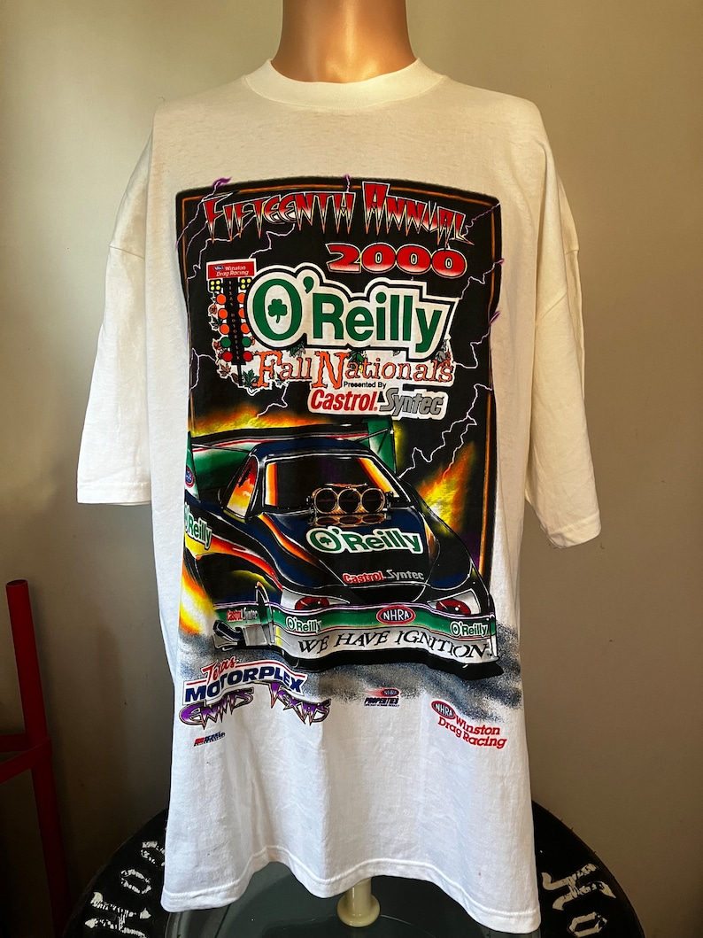 May include: White t-shirt with a graphic print of a drag racing car. The graphic features the text "2000 O'Reilly Fall Nationals Presented by Castrol Syntec" and "We Have Ignition".