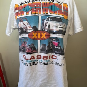 May include: White t-shirt with a colorful graphic of race cars and the text "SKOAL BANDIT RACING COPPER WORLD 1995 CHAMPIONS XIX CLASSIC FEBRUARY 2-4, 1996  POINTERNATIONAL RACEWAY."